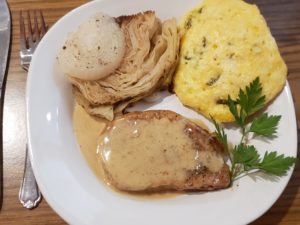 Baked Cabbage and Onions with biscuit and pork chop on a white plate